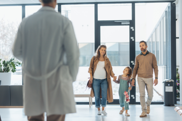 Girl patient looking forward to her doctor and examination in a modern clinic. Girl arriving in hospital with her parents. Emotional support during medical examination in hospital.