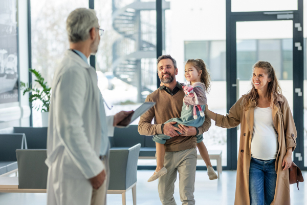 Girl patient looking forward to her doctor and examination in a modern clinic. Girl arriving in hospital with her parents. Emotional support during medical examination in hospital.