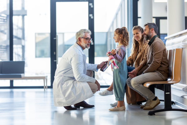 Doctor explaining results of MRI scan of brain to parents of young girl patient, delivering good news. Diagnosis of diseases and head injuries. Concept of children healthcare and emotional support for child patients.