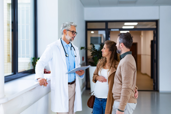 Pregnant woman and husband talking to obstetrician in hospital. Admitting woman in labor to maternity ward, planned cesarean section.