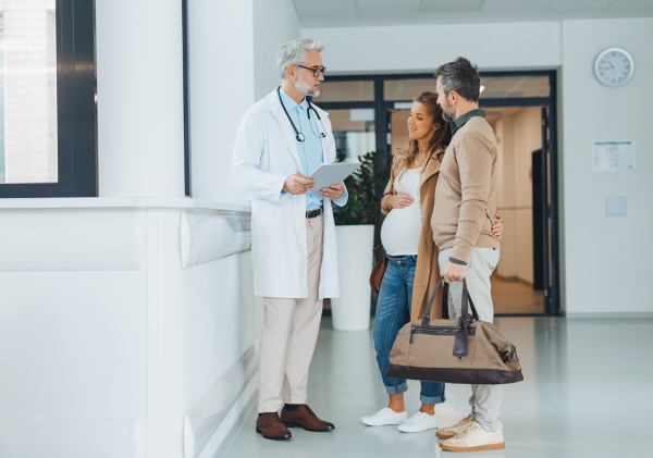 Pregnant woman and husband talking to obstetrician in hospital. Admitting woman in labor to maternity ward, planned cesarean section.