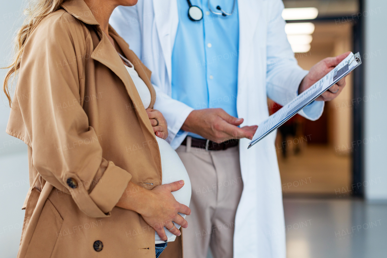 Close up of pregnant woman talking to obstetrician in hospital, holding her pregnant belly. Doctor and future mother discussing childbirth, planned cesarean section, epidural.