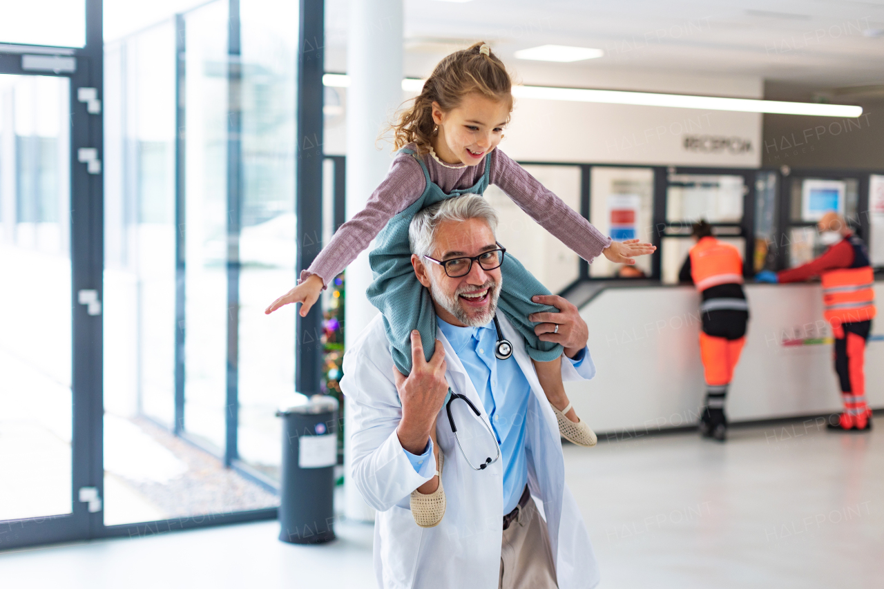 Portrait of a pediatrician with a little patient sitting on his shoulders, piggyback. Doctor carrying girl on shoulders. Friendly relationship between the doctor and the child patient.