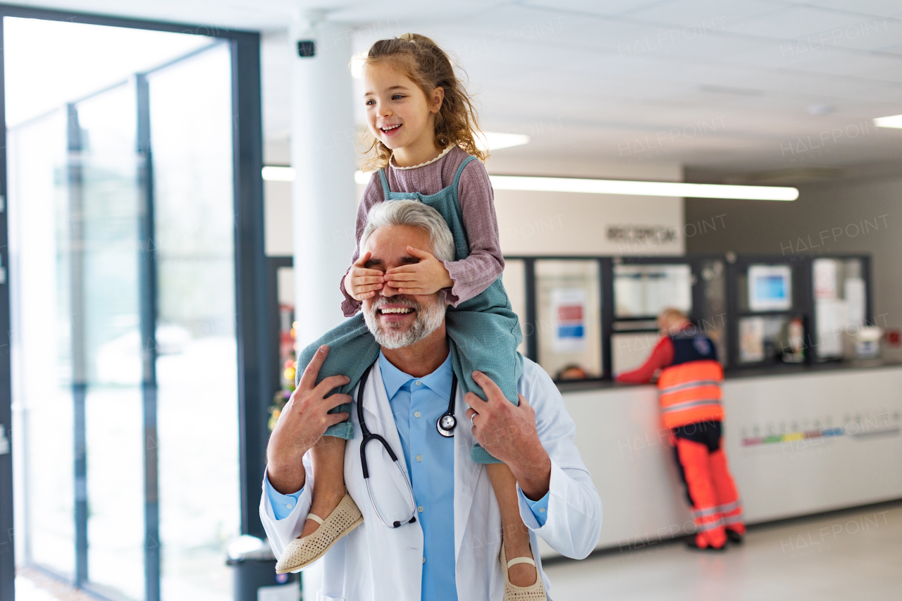 Portrait of a pediatrician with a little patient sitting on his shoulders, piggyback. Doctor carrying girl on shoulders. Friendly relationship between the doctor and the child patient.