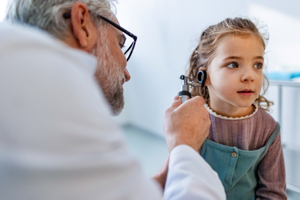 Close up of doctor examining little girl's ear using otoscope, looking for infection. Friendly relationship between the doctor and the child patient.