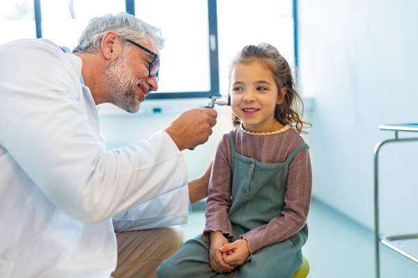 Close up of doctor examining little girl's ear using otoscope, looking for ear infection. Friendly relationship between the doctor and the child patient.