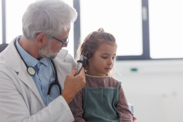 Close up of doctor examining little girl's ear using otoscope, looking for infection. Friendly relationship between the doctor and the child patient.