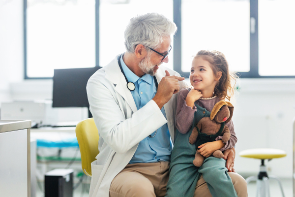 Portrait of a pediatrician with a little girl patient sitting on his knee. Friendly relationship between the doctor and the child patient.