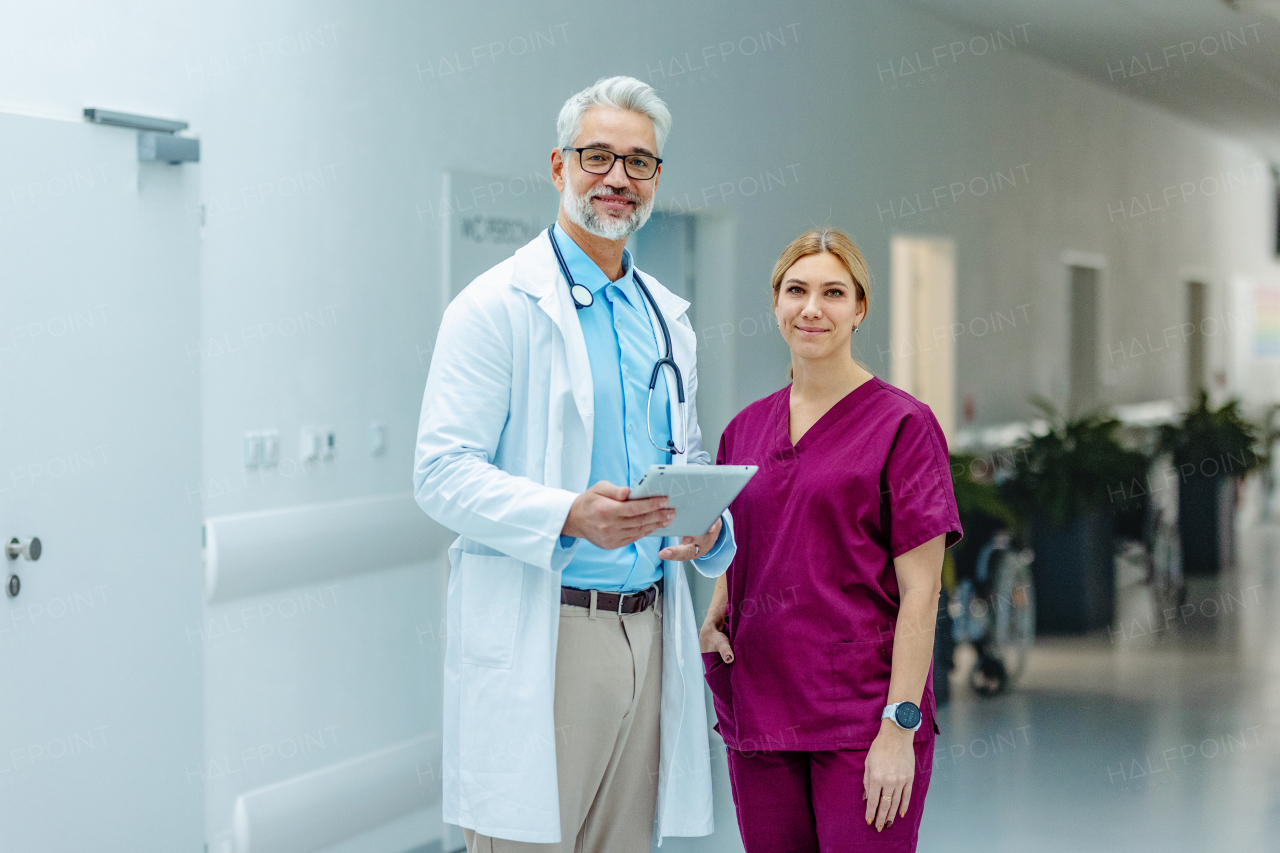 Portrait of medical team, doctor and beautiful nurse in uniform, standing in the hospital corridor, looking at the camera and smiling.