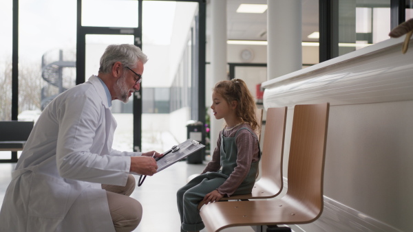 Friendly pediatrician talking to little patient. Cute preschool girl with doctor in hospital corridor. Concept of children healthcare and emotional support for child patients.