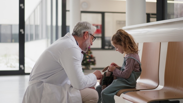 Friendly pediatrician talking to little patient. Cute preschool girl with doctor in hospital corridor. Concept of children healthcare and emotional support for child patients.