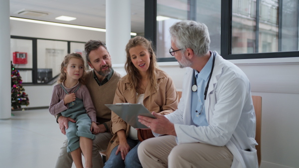 Doctor explaining results of MRI scan of brain to parents of young girl patient, delivering good news. Diagnosis of diseases and head injuries. Concept of children healthcare and emotional support for child patients.