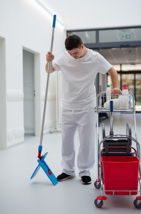 Young man with down syndrome working in hospital as cleaner. Concpet of integration people with disability into society.