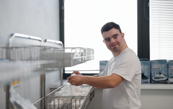 Young man with down syndome working in a hospital as helper. Concept of integration people with disability into society.