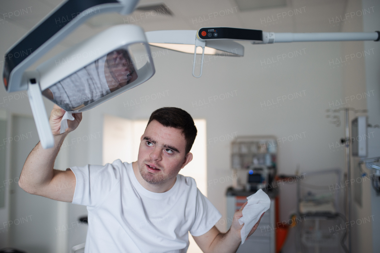 Young man with down syndome working in a hospital as helper, cleaner. Concpet of integration people with disability into society.