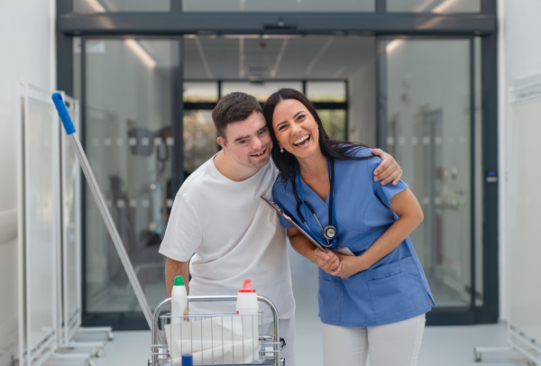 Young man with down syndrome working in hospital as cleaner, talking to nurse, having fun. Concpet of integration people with disability into society.