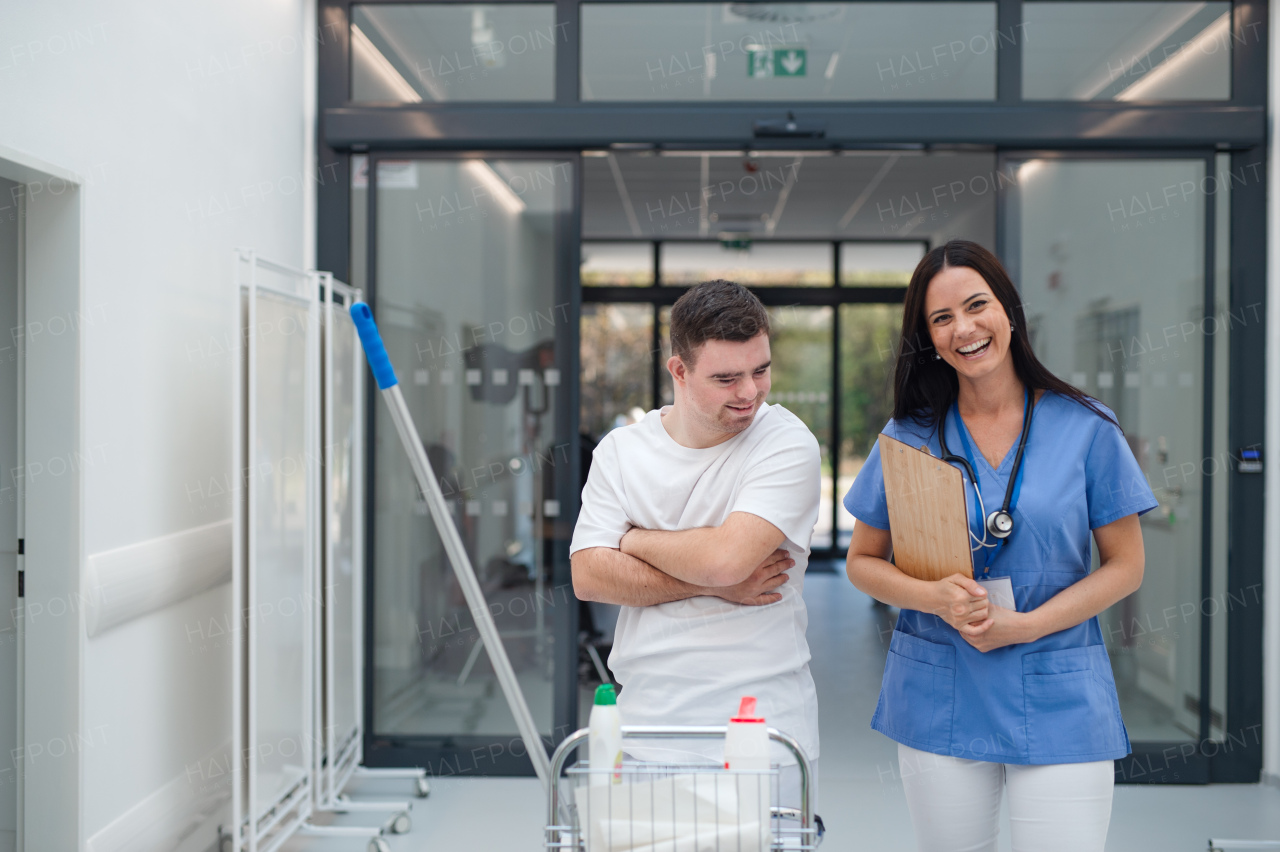 Young man with down syndrome working in hospital as cleaner, talking to nurse, having fun. Concpet of integration people with disability into society.