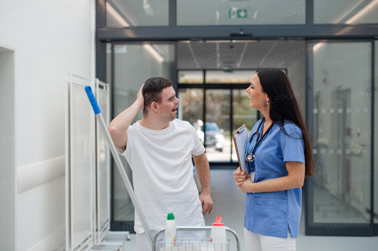 Young man with down syndrome working in hospital as cleaner, talking to nurse, having fun. Concpet of integration people with disability into society.