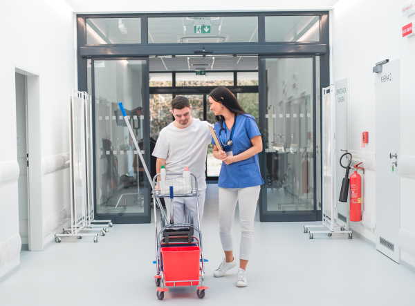 Young man with down syndrome working in hospital as cleaner, talking to nurse, having fun. Concpet of integration people with disability into society.