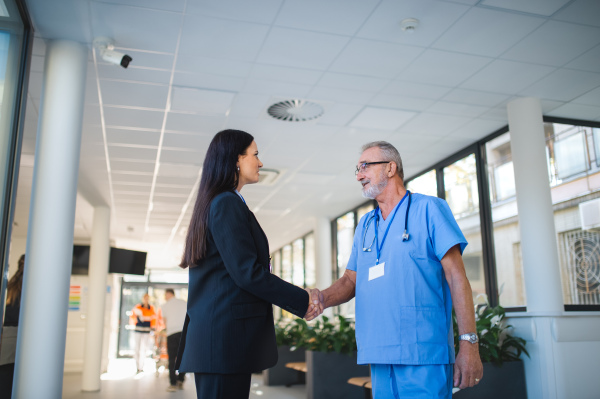 Young business woman shaking hand with elderly doctor in a hospital room.