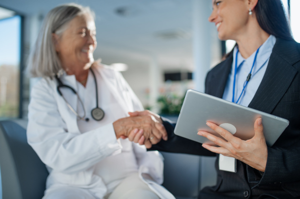 Young business woman shaking hand with elderly doctor in a hospital room.