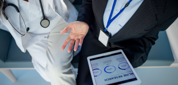 High angle view of business woman showing chart on digital tablet to doctor in hospital.