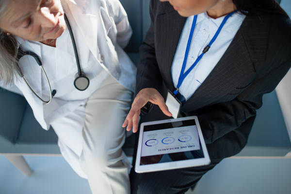 High angle view of business woman showing chart on digital tablet to doctor in hospital.