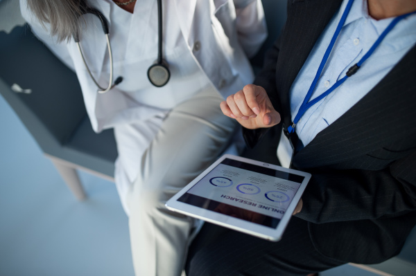 High angle view of business woman showing chart on digital tablet to doctor in hospital.