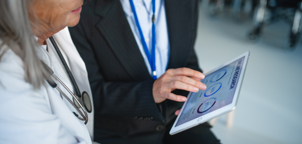 High angle view of business woman showing chart on digital tablet to doctor in hospital.