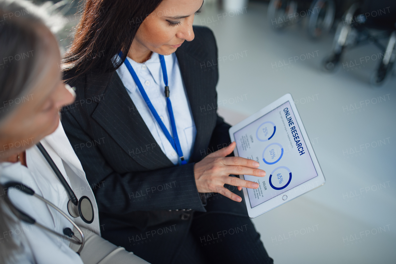 High angle view of business woman showing chart on digital tablet to doctor in hospital.