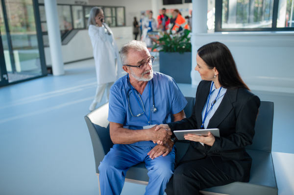 Young business woman shaking hand with elderly doctor in a hospital.