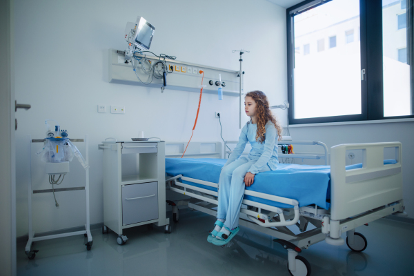 Little sick girl sitting alone in a hospital ward.