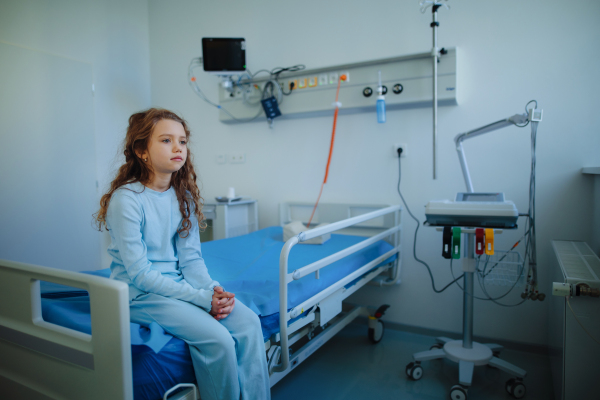 Little sick girl sitting alone in a hospital ward.