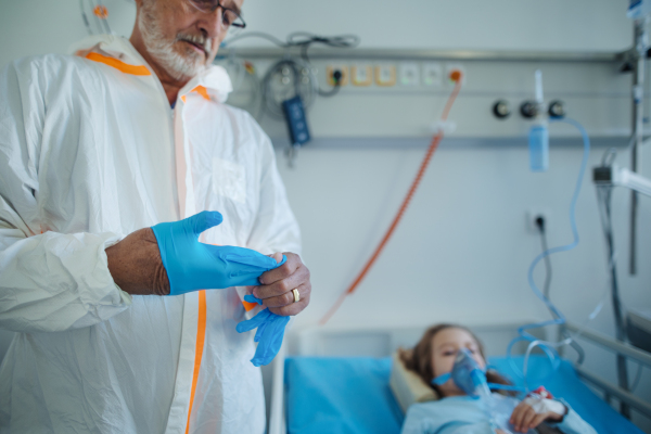 Doctor in protective coverall putting off surgical gloves after examination of little girl.