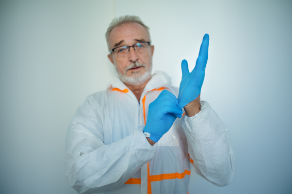 Portrait of doctor in a protective coveral putting on surgical gloves.