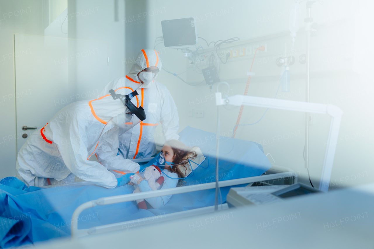 Little girl with an infection disease lying in hospital room, doctors in protective coverals examining her.