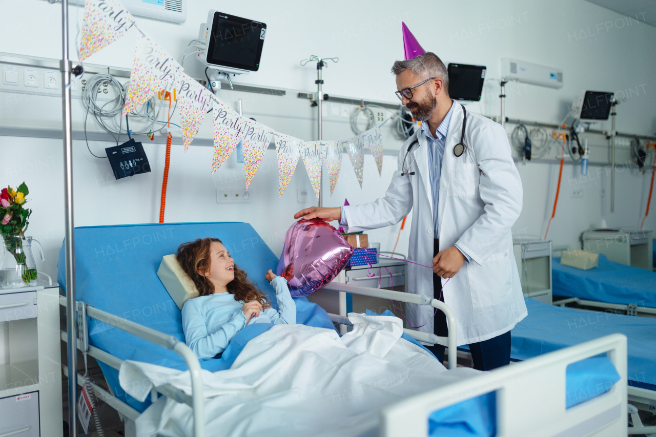 Happy doctor celebrating birthday with little girl in a hospital room.