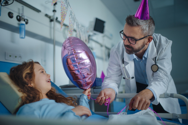 Happy doctor celebrating birthday with little girl in a hospital room.