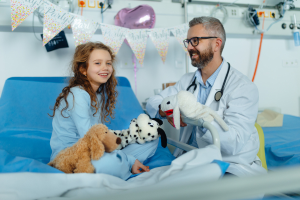 Happy doctor celebrating birthday with little girl in a hospital room.