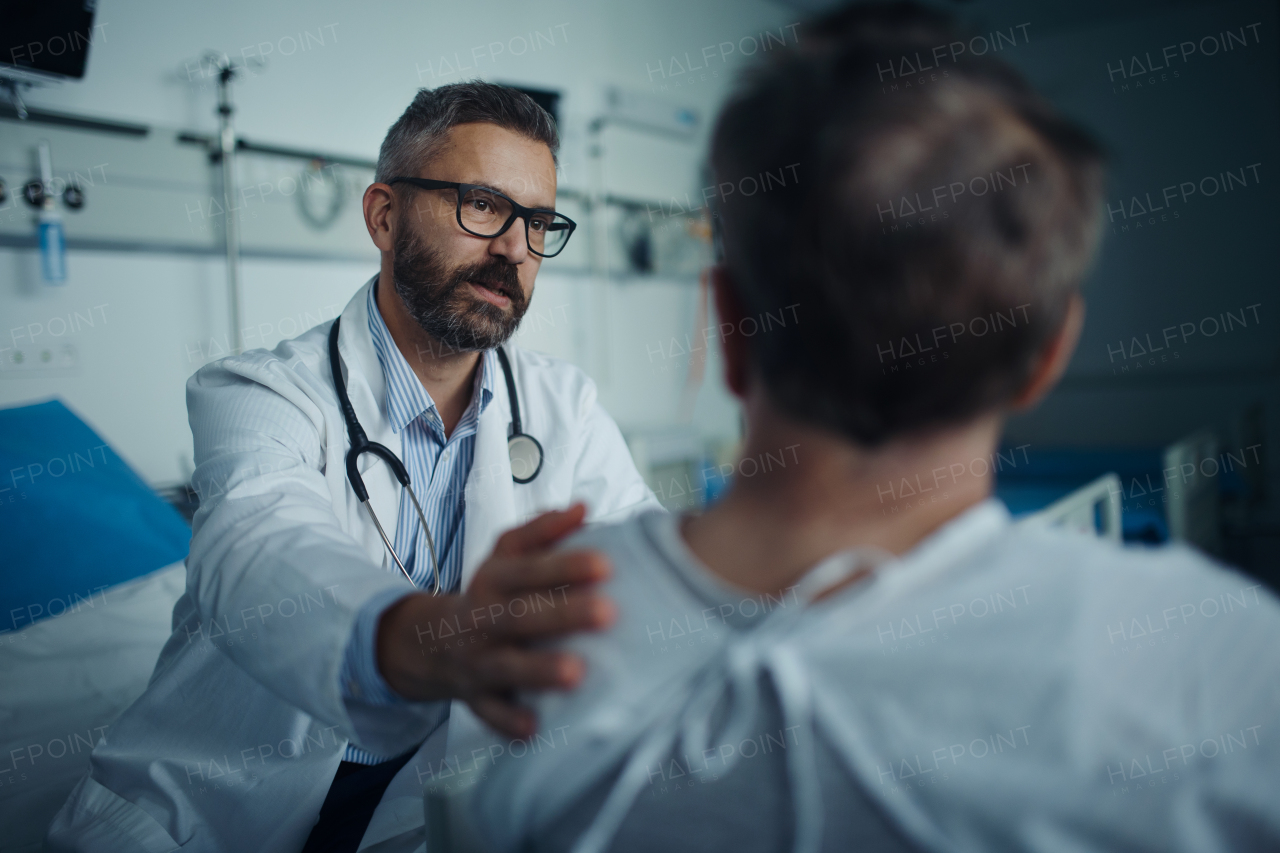 Mature doctor consoling and explaining diagnosis to his patient in hospital room.