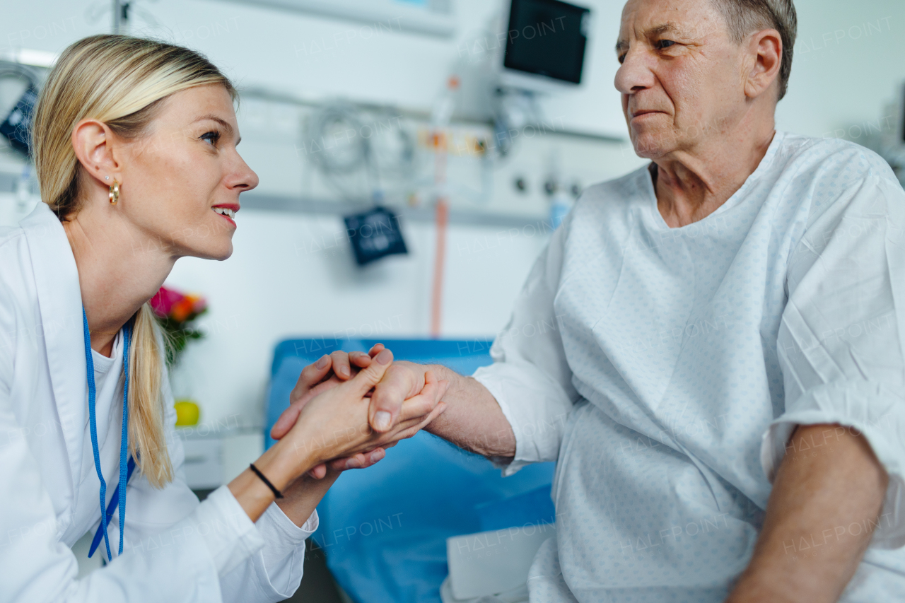 Young woman doctor holding hand, and talking with her patient in hospital room.