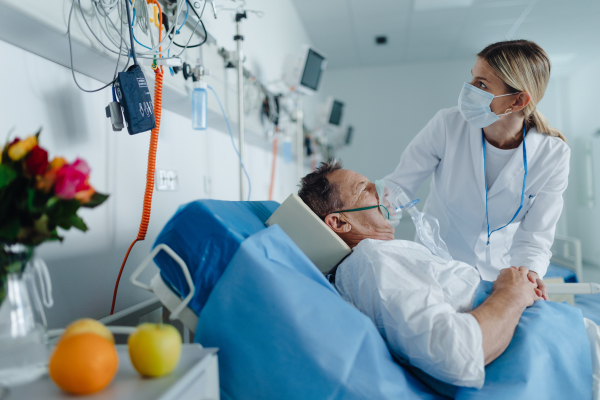 Young woman doctor checking elderly patient with oxygen mask in coma.