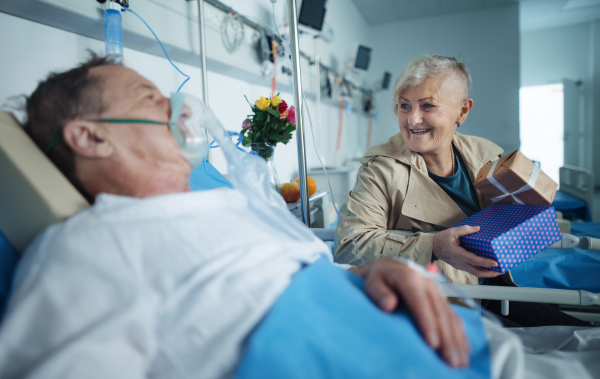 Senior woman visiting her husband in hospital, bringing him gifts.