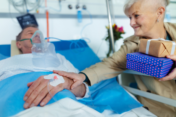 Senior woman visiting her husband in hospital, bringing him gifts.