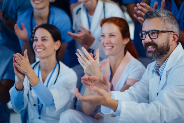 Portrait of happy doctors, nurses and other medical staff clapping, in a hospital.