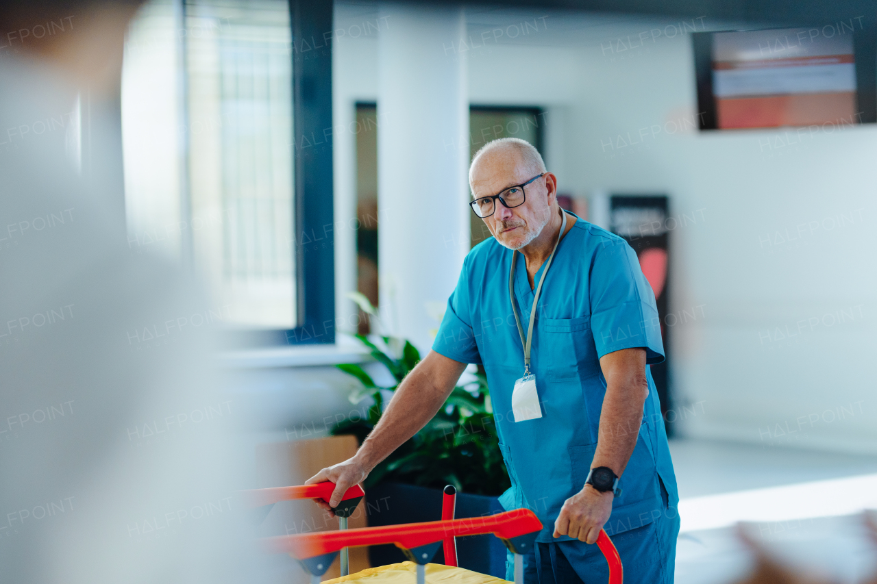 Elderly caregiver pushing hospital bed at a corridor.