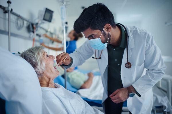 Young doctor examining throat to senior patient in a hospital room.