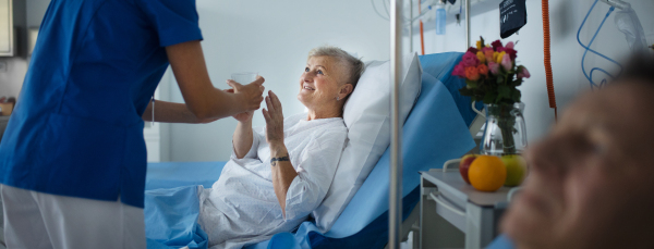 Young nurse giving glass of water to senior patient at a hospital ward.