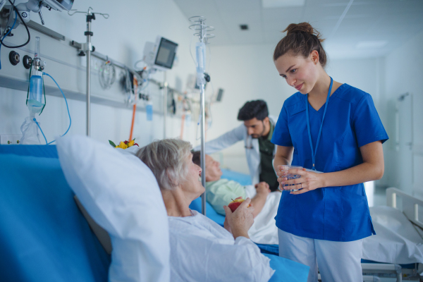 Young nurse giving glass of water to senior patient at a hospital ward.