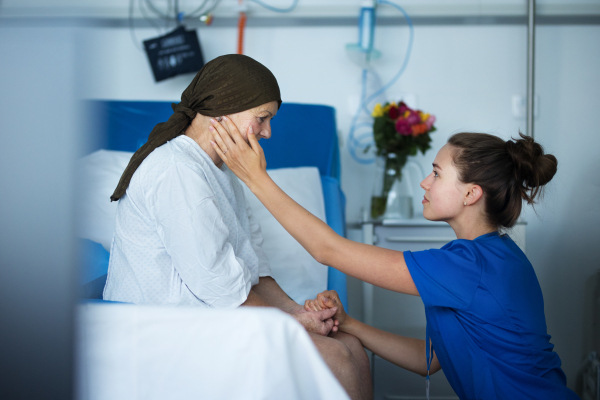 Empathic nurse taking care of a senior woman with cancer, stroking her cheek.